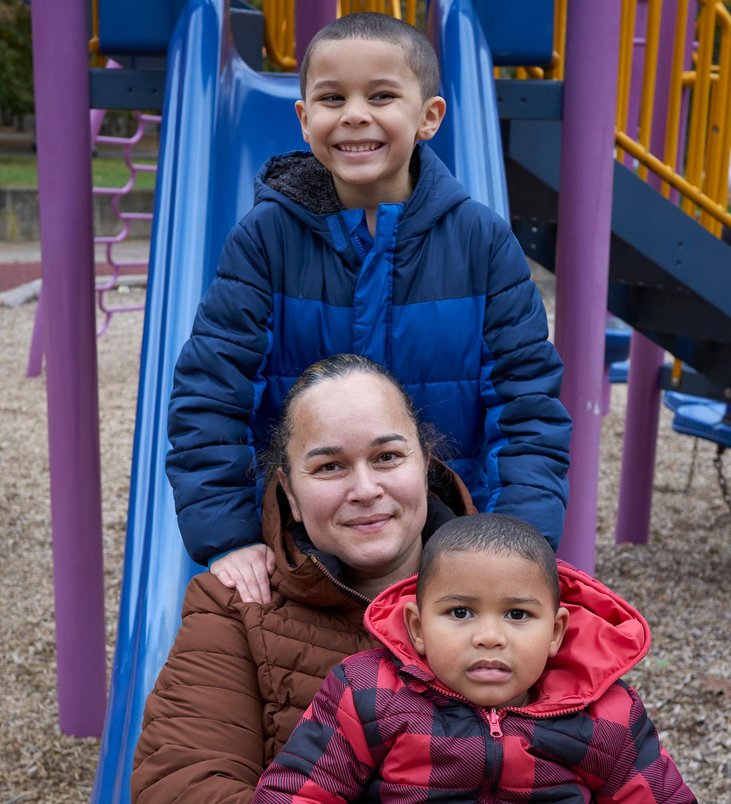 Mother_poses_with_her_two_young_sons_sitting_at_a_park Mother poses with her two young sons sitting at a park