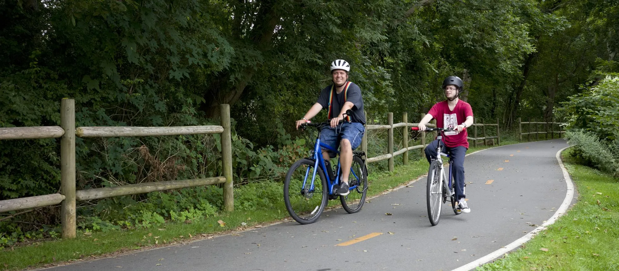 Two young men riding on a tree lined bike path