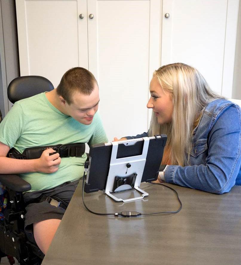 Young man using wheelchair looks at tablet with staff person