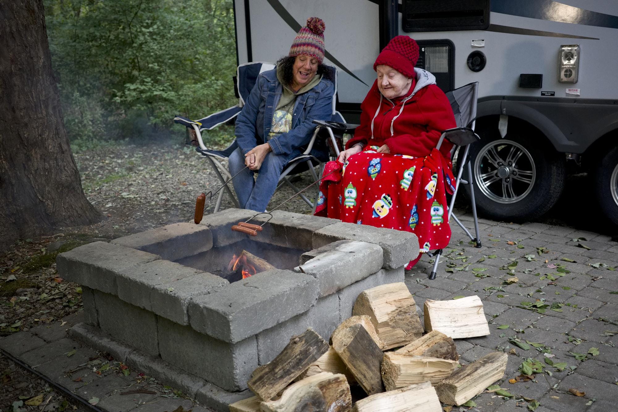 Two women chat as they roast hotdogs at a campfire