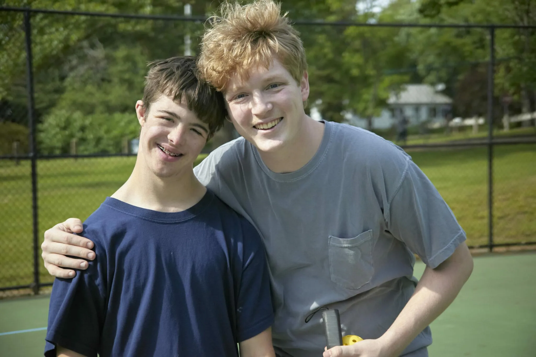 Smiling teenaged boy with young staff person on pickleball court