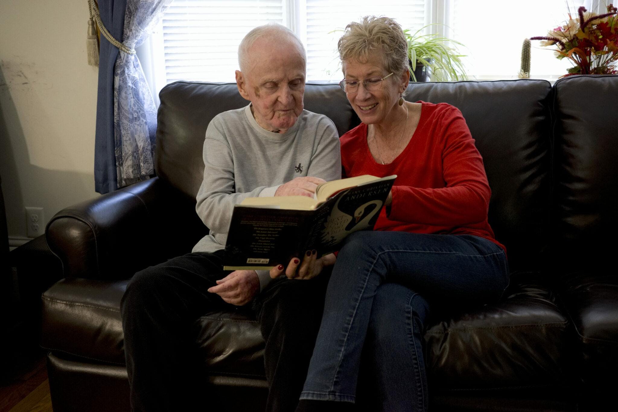 Two people sitting on living room couch reading book together