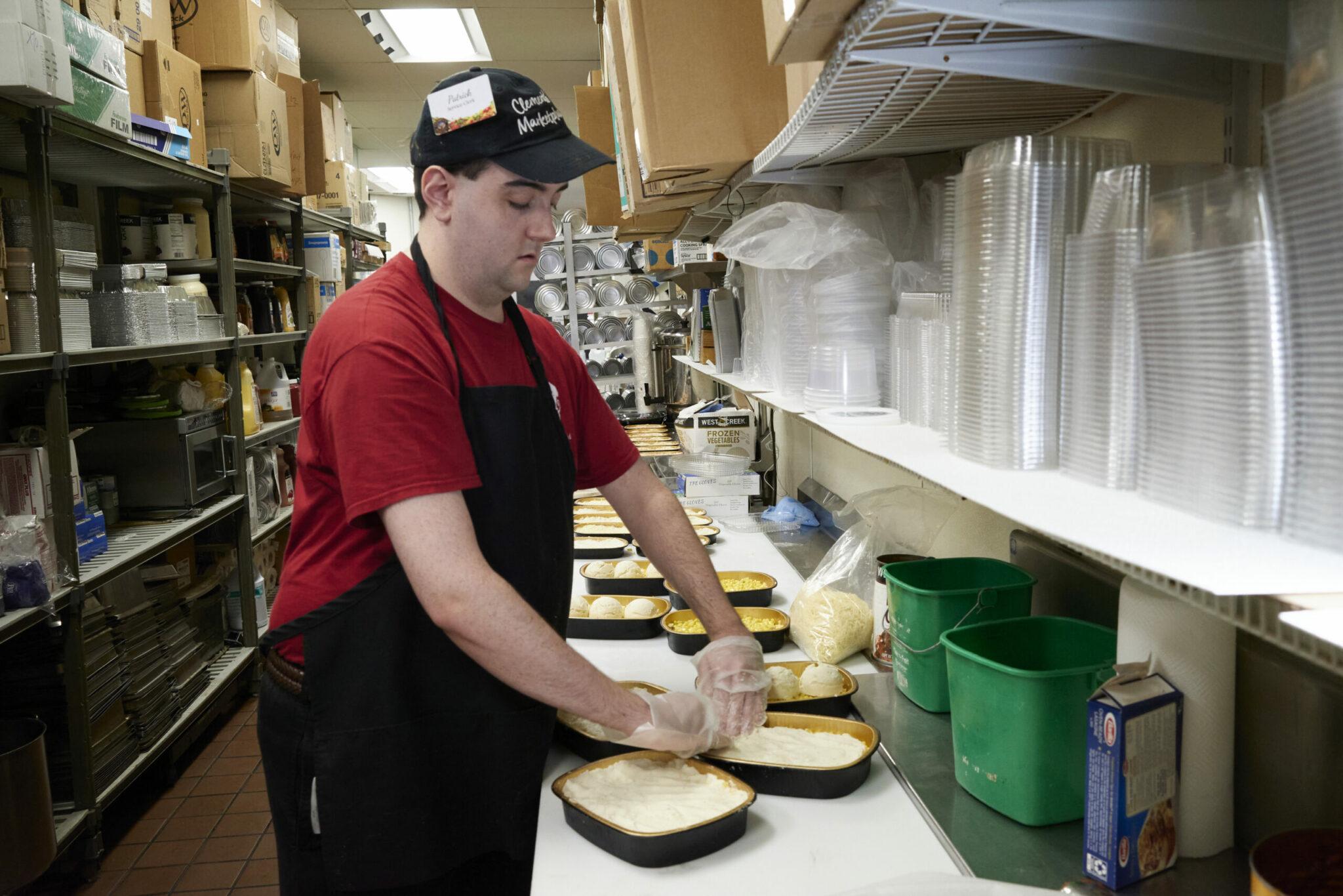 Young man at counter creating pre-prepared meals for deli