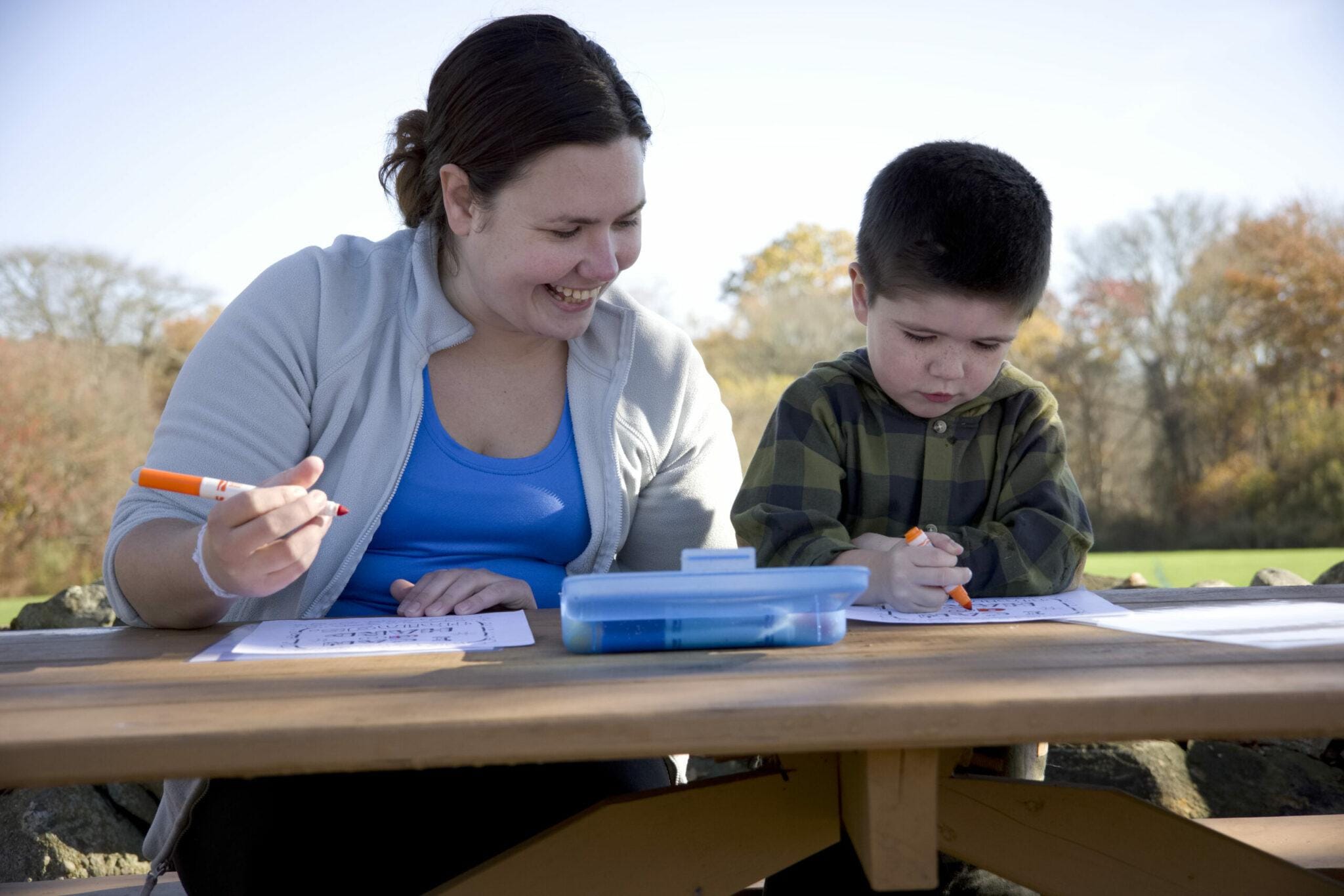 Young woman and little boy coloring in the park.