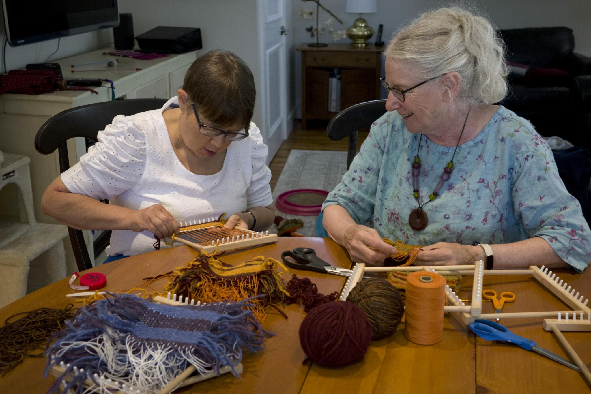 Young woman weaves while smiling volunteer looks on