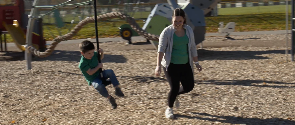 Boy has fun on zip line at park while young woman cheers him on