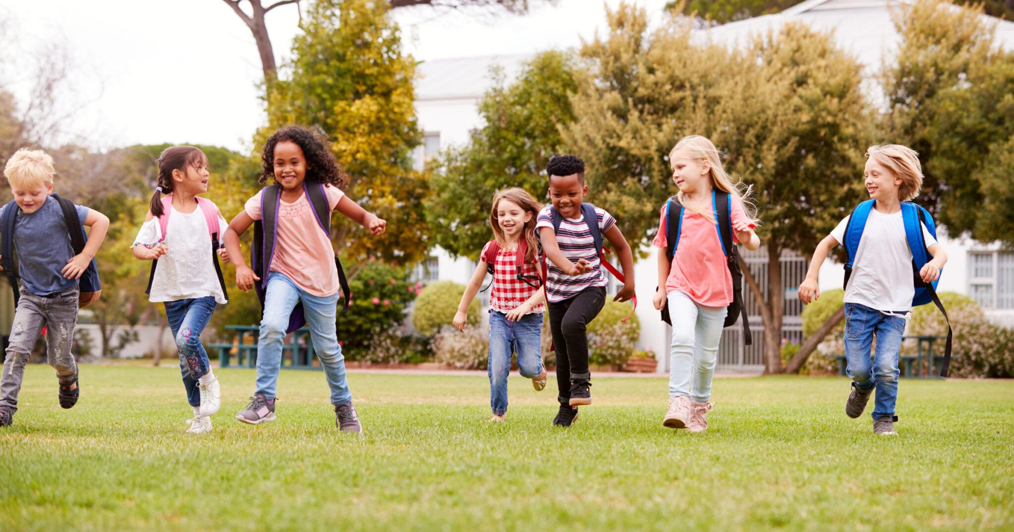 Smiling grade school students with backpacks running outdoors