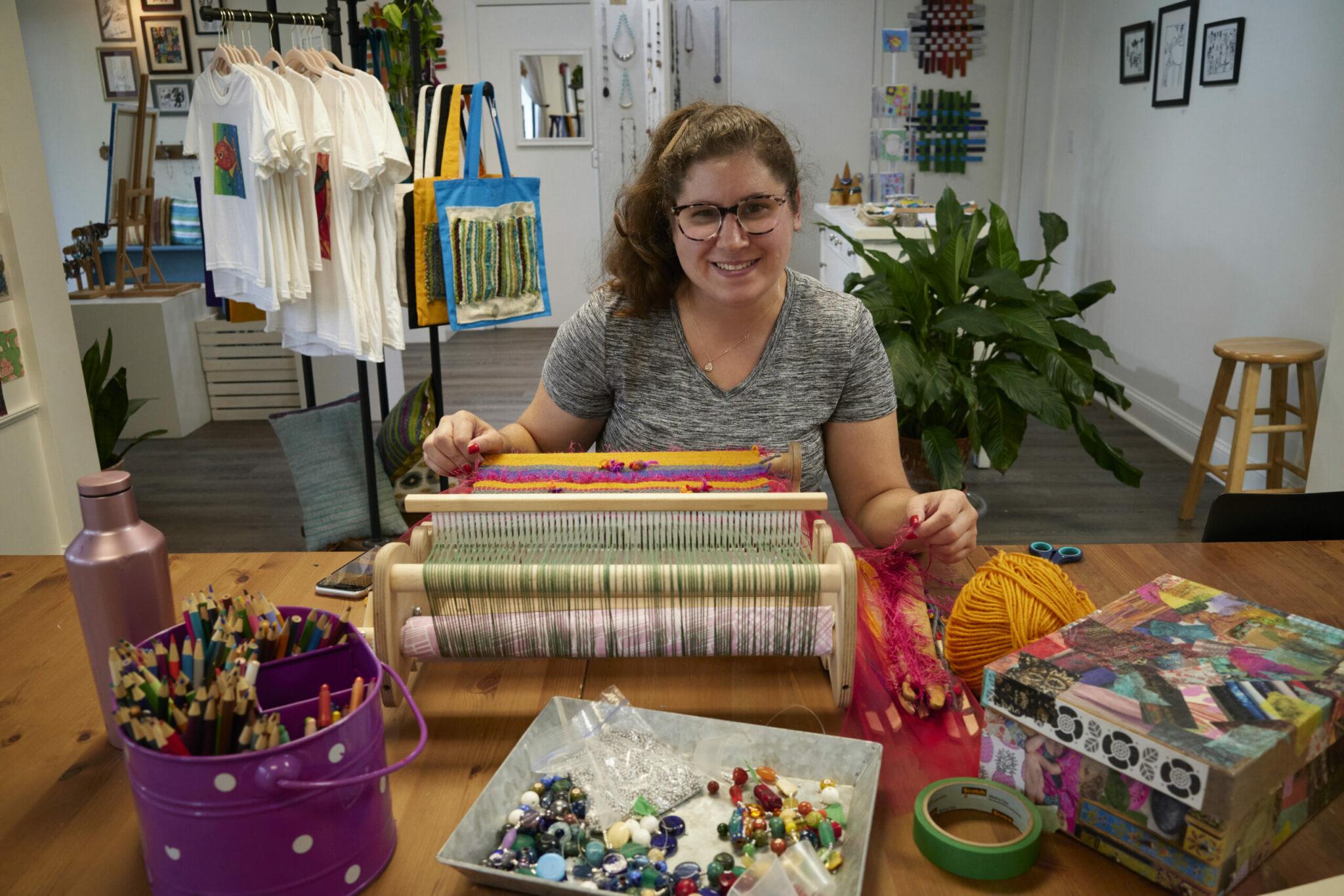 Young woman in storefront at a loom weaving