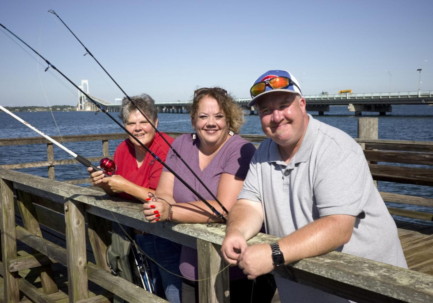 Three people fishing together off a pier with Newport Bridge in background