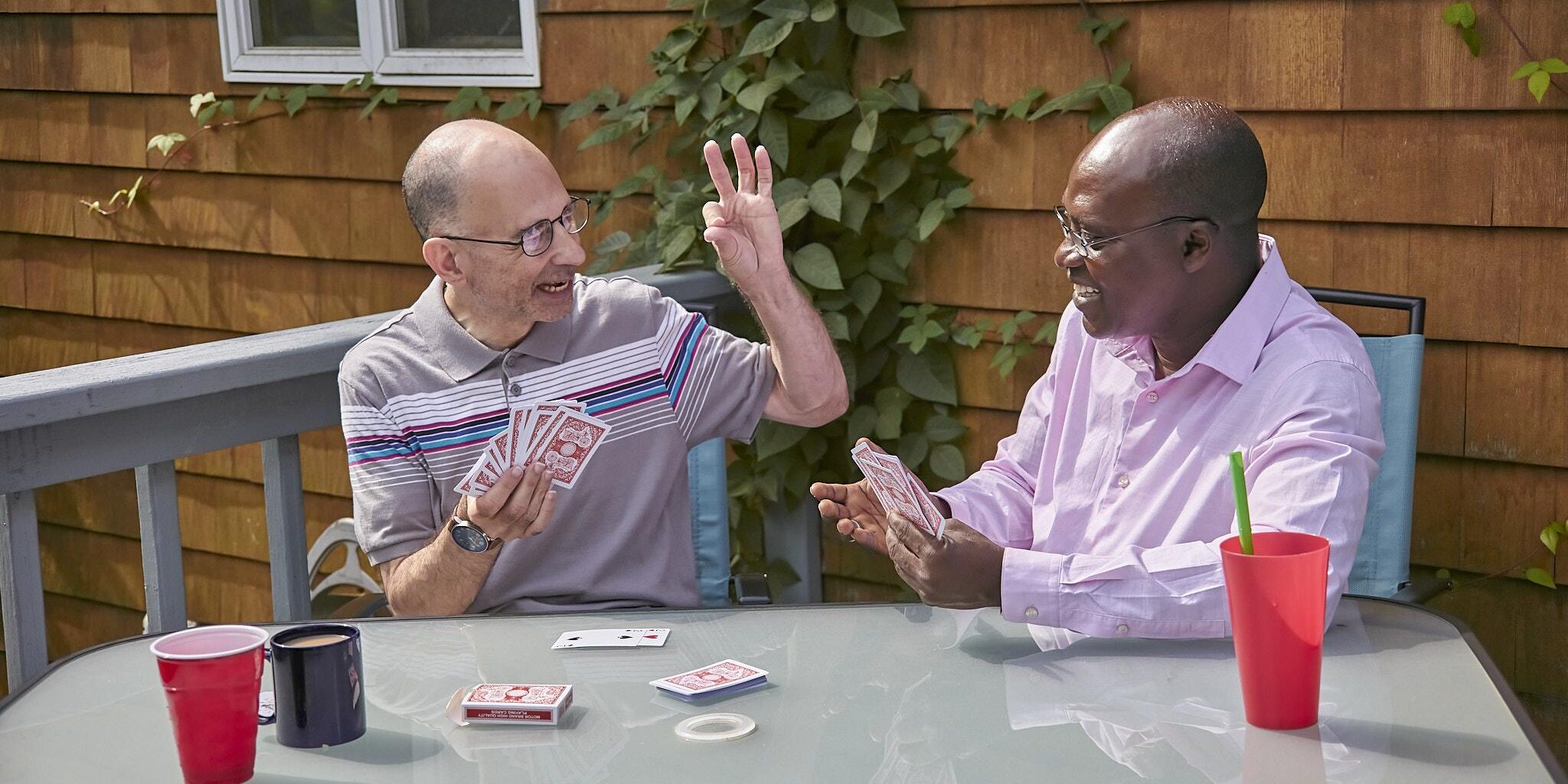 Two men playing cards sitting on a sunny patio