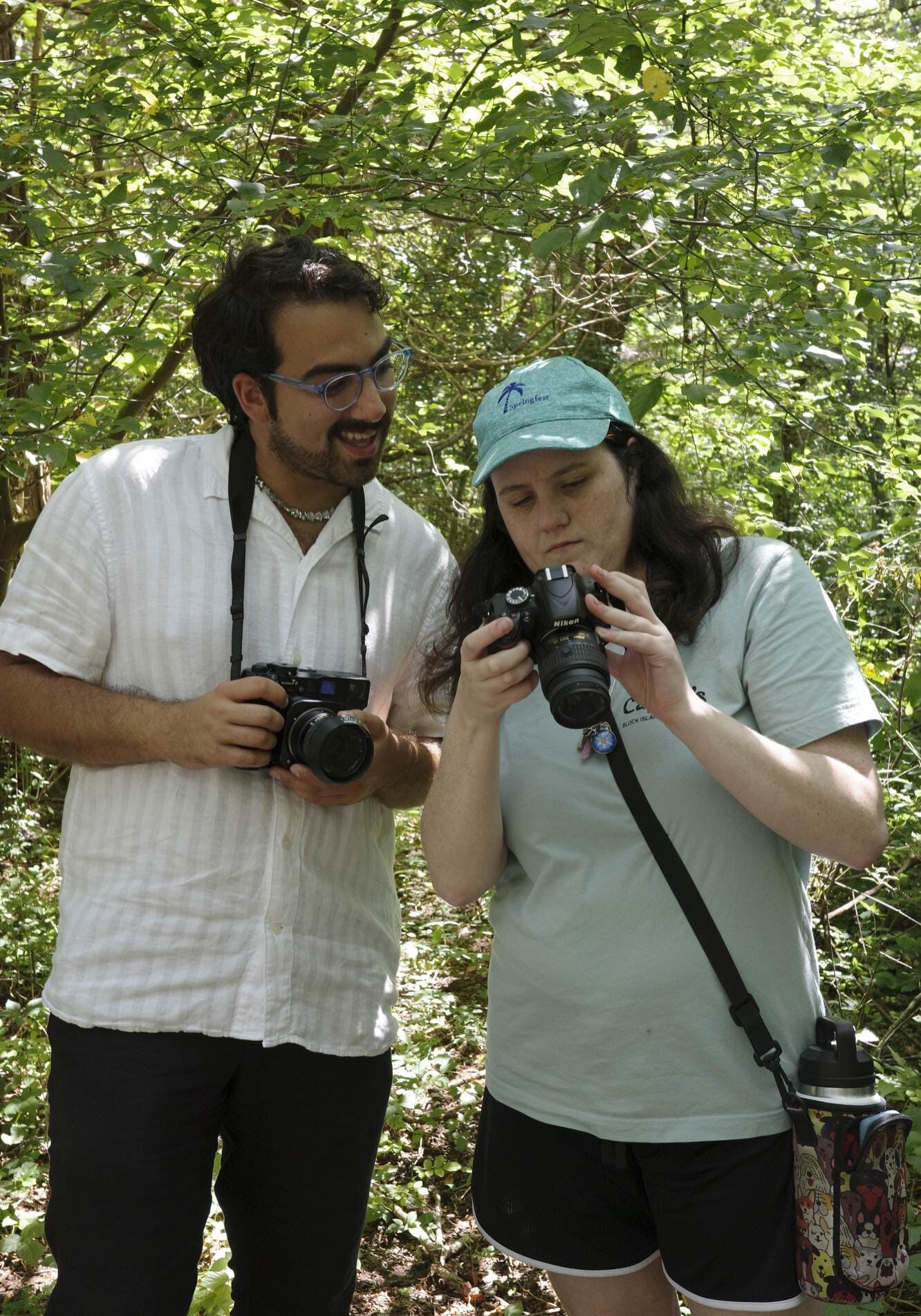While out in the woods, young woman shares images on her camera with fellow photographer