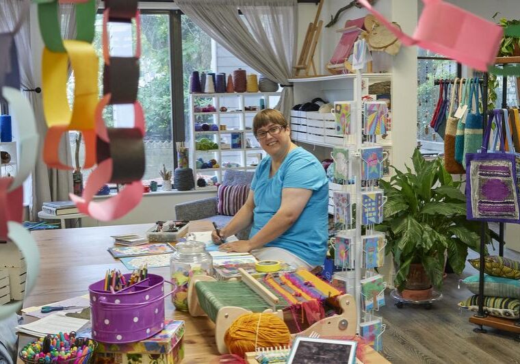 3 Unique Art Studios Young artist sits at table drawing in a colorful gallery with greeting cards woven handbags and pillow on display
