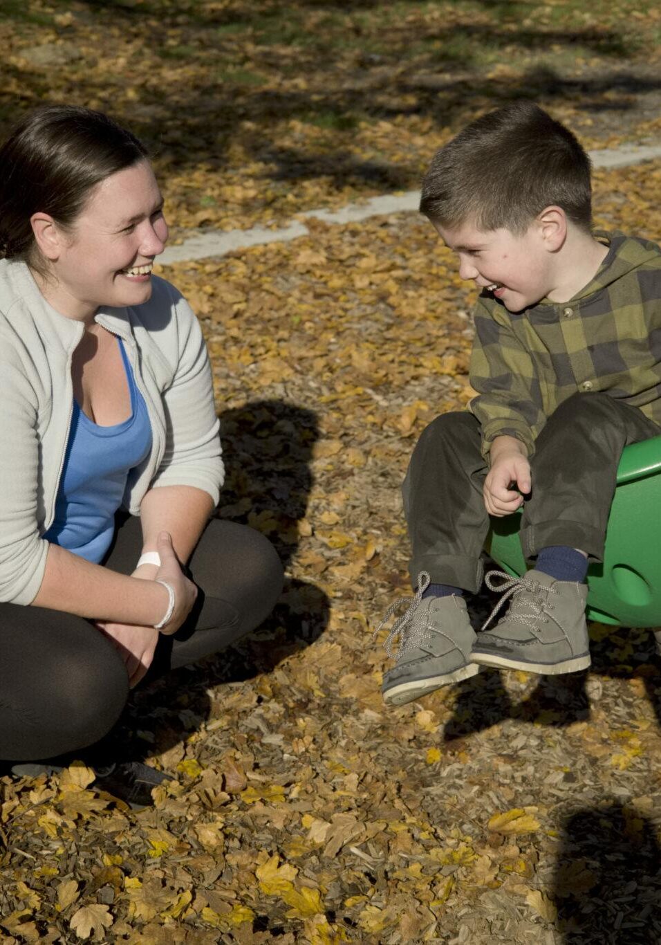 Young woman face to face and smiling at small boy on playground