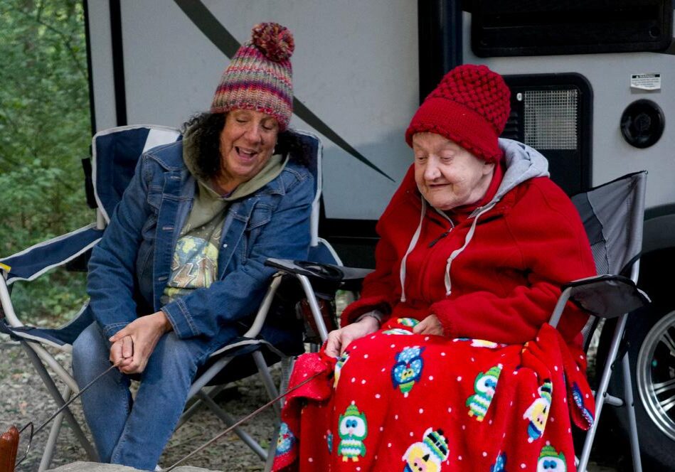 Two women chat as they roast hot dogs at a campfire